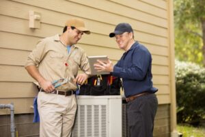 Two technicians working on an air conditioner outside the home.