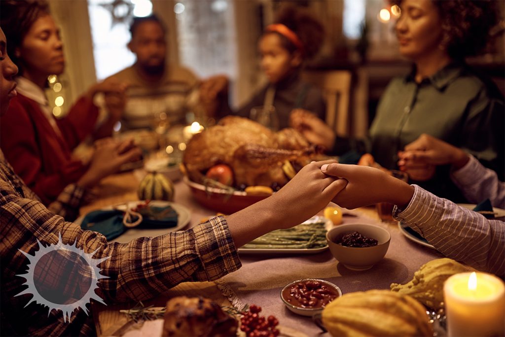 A black family gathered and holding hands over a Thanksgiving meal.